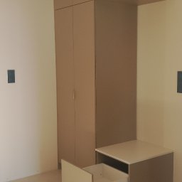 Meble Rycerski - Beżowa szafa z otwartą szufladą w minimalistycznym wnętrzu. Proste linie, jasne kolory, nowoczesny design. Widoczne detale wykończenia i oświetlenie sufitowe.