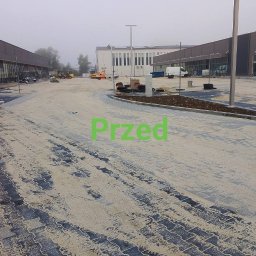 RKubica mycie cisnieniowe - Rozległy plac z kostki brukowej w trakcie budowy, z widocznymi maszynami budowlanymi w tle i elementami infrastruktury. Ujęcie w pochmurny dzień.