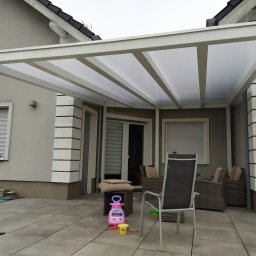 FSR SERHII REUTSKYI - Biała pergola z poliwęglanowym dachem nad tarasem z szarych płyt. Widoczne meble ogrodowe i zabawki dziecięce. Nowoczesna konstrukcja przydomowa.