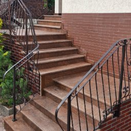 M&R Spółka z ograniczoną odpowiedzialnością - Eleganckie schody zewnętrzne z polerowanego brązowego granitu, z ozdobnymi kutymi balustradami i ceglaną podmurówką, prowadzące do wejścia domu.