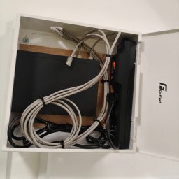 Primeron Sp. z o.o. - Zamknięta skrzynka z zamontowanym routerem, listwą zasilającą i okablowaniem sieciowym. Widoczne kable Ethernet i zasilające, listwa zasilająca GetFort.