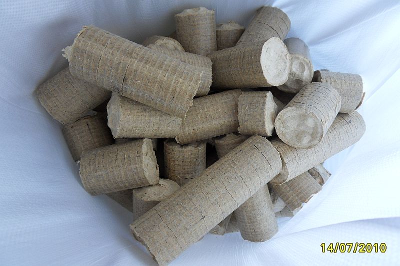 Stos cylindrycznego brykietu drzewnego w worku z białego materiału, widoczny delikatny wzór tekstury brykietów.