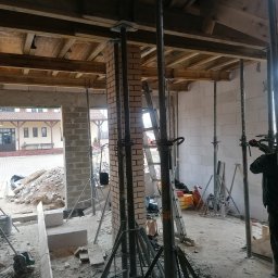 Cw Budownictwo - Wnętrze w trakcie budowy: widoczne podpory stropowe, ściany z bloczków i cegieł, narzędzia budowlane. Ujęcie z perspektywy osoby stojącej wewnątrz budynku.