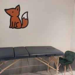 Leśne Słówka - Gabinet z kozetką do terapii manualnej, krzesłem i naklejką lisa na ścianie. Jasne wnętrze, neutralne kolory, minimalistyczny wystrój. Przytulna atmosfera.