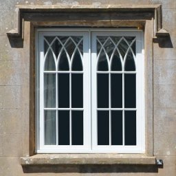 Timber Windows - Białe okno drewniane z ozdobnymi szprosami w kamiennej fasadzie budynku w Skarbimierzu Osiedle. Klasyczny design, symetryczny układ.