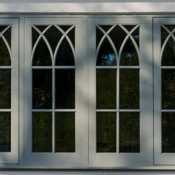 Timber Windows - Czteroskrzydłowe okno z ozdobnymi szprosami w stylu gotyckim, osadzone w białej, teksturowanej ścianie. Delikatne cieniowanie podkreśla fakturę.