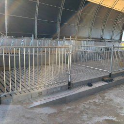 Agro AMA Sp. z o.o. - Metalowe ogrodzenie z rur wewnątrz zadaszonej konstrukcji, prawdopodobnie w obiekcie rolniczym. Widoczne narzędzia ślusarskie.