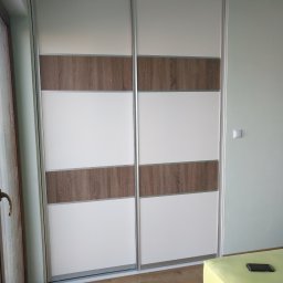 LUXURY FURNITURE - Dwudrzwiowa szafa przesuwna z białymi i drewnopodobnymi panelami, widoczna w rogu sypialni z drewnianą podłogą i fragmentem łóżka z telefonem.