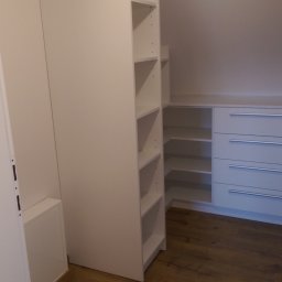 LUXURY FURNITURE - Biała szafa wnękowa z półkami i szufladami, dopasowana do skosu dachu na poddaszu. Widoczna drewniana podłoga i metalowy drążek na ubrania.