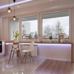 LUXURY FURNITURE - Jasna kuchnia z oknem na balkon. Białe meble, drewniany blat, heksagonalne płytki. Stół z tulipanami, oświetlenie LED pod parapetem. Widok na miasto zza okna.