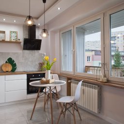 LUXURY FURNITURE - Jasna kuchnia z białymi meblami i drewnianym blatem. Na stole tulipany w wazonie. Za oknem widok na osiedle. Minimalistyczny design z akcentami roślinnymi.