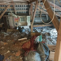 Ekipa Szybkiego Sprzątania - Zabrudzone poddasze ze stertą śmieci, workami i starymi meblami. Widoczne drewniane elementy konstrukcyjne dachu i fragmenty instalacji elektrycznej.
