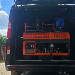 Flush czyszczenie kanalizacji - Profesjonalna maszyna wysokociśnieniowa z niebieskim wężem na bębnie i panelami sterowania, zamontowana w otwartym bagażniku czarnego vana, gotowa do pracy.