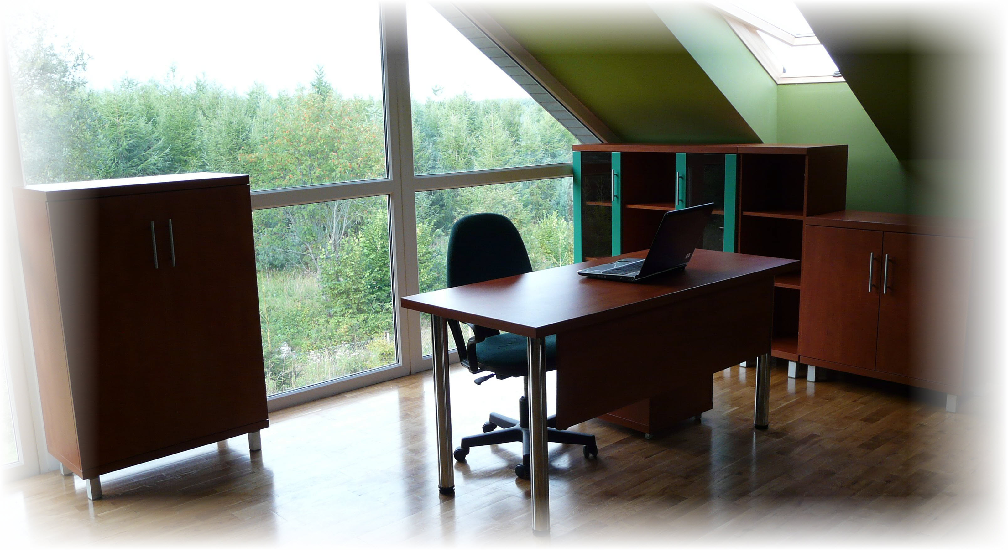 Komplet mebli biurowych z biurkiem i szafkami w odcieniach brązu, z laptopem na blacie, na tle dużego okna z widokiem na las.