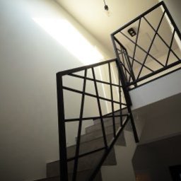 MetalCraft - Nowoczesna, czarna balustrada schodowa z geometrycznym wzorem krzyżujących się linii, oświetlona naturalnym światłem wpadającym z góry.