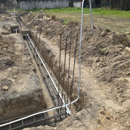 Elflow Maciej Zawiasa - Uziemienie budynku w trakcie realizacji: wykop z płaskownikiem ocynkowanym i prętami uziemiającymi, widoczne punkty wyprowadzone do rozdzielni i instalacji odgromowej.