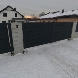 DM STEEL Sp. z o. o. - Antracytowe ogrodzenie posesji z poziomymi panelami i jasnymi słupkami, z furtką i domofonem, na tle zaśnieżonego podwórka i domów.