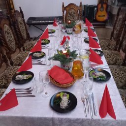 Tawerna Kuternoga - Uroczysty stół z nakryciami, czerwonymi serwetkami i potrawami na czarnych talerzach. W tle pianino, akordeon i gitara. Dekoracja świąteczna ze świecą.