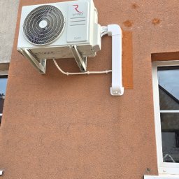 Usługi Hydrauliczne RAWEX - Zamontowany klimatyzator Rotenso Hiro na elewacji budynku, z widocznymi elementami instalacji odprowadzającej skropliny. Ujęcie z boku, w dziennym świetle.