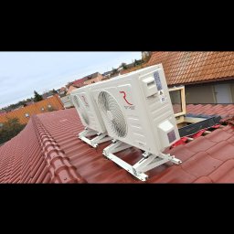 Usługi Hydrauliczne RAWEX - Dwa białe klimatyzatory marki Rotenso zamontowane na specjalnych wspornikach na czerwonym, spadzistym dachu budynku. Widok z góry, w tle zabudowa mieszkalna.
