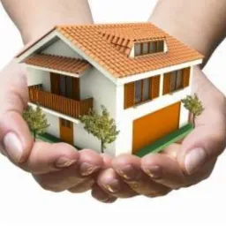 Model domu z pomarańczowym dachem, trzymany w dłoniach na białym tle. Prezentacja projektu domu z garażem i balkonem.