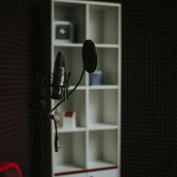FMD.studio - Mikrofon studyjny z pop filtrem i słuchawkami w wyciszonym pomieszczeniu, na tle białego regału. Sprzęt audio w profesjonalnym studio nagrań.