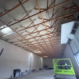 AlfaPur Ocieplenia Pianą Pur - Poddasze po ociepleniu pianką PUR, widoczne drewniane krokwie i instalacje. Na podłodze resztki materiałów budowlanych i podnośnik koszowy.