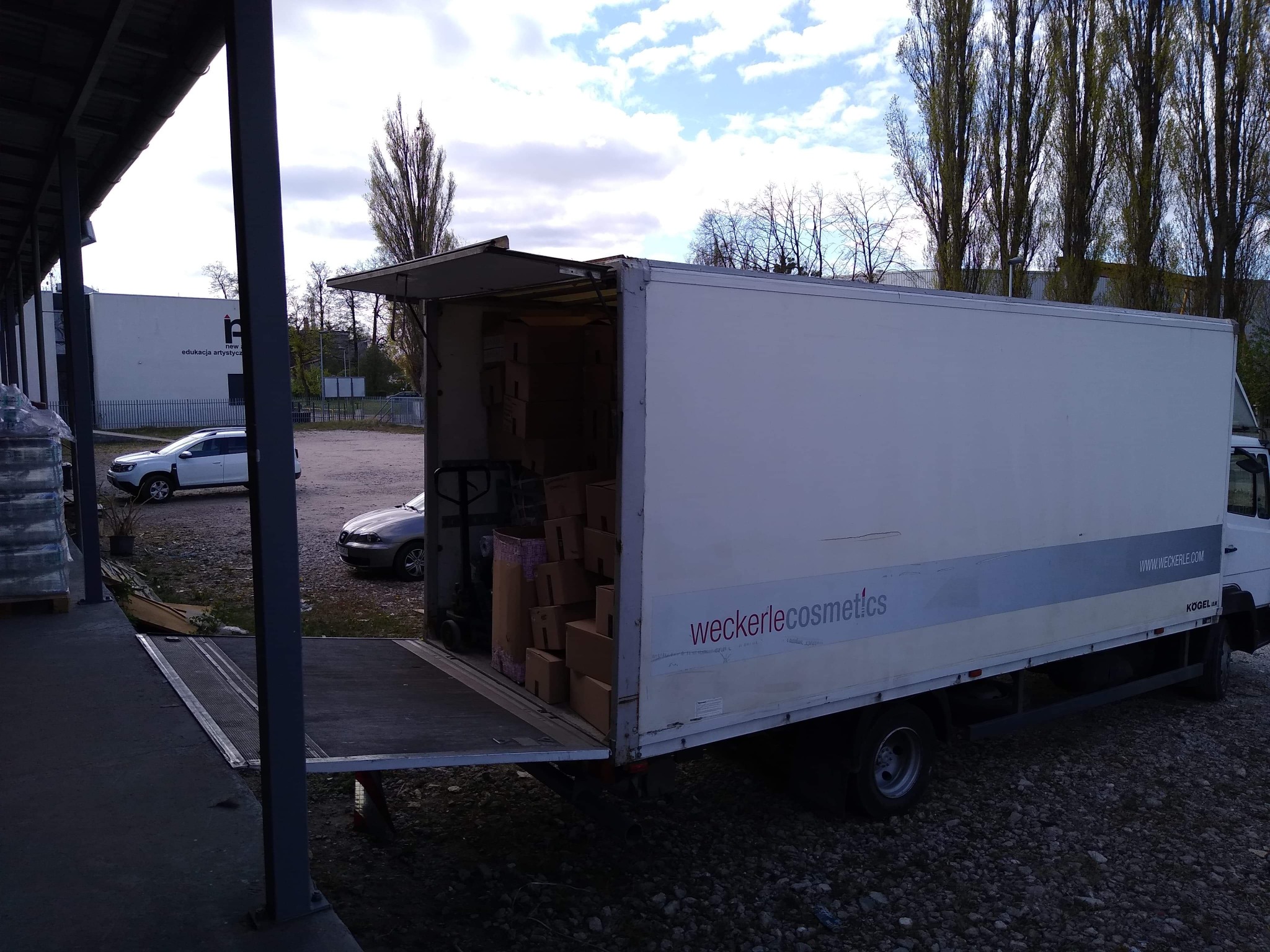 Ciężarówka z otwartą paką, załadowana kartonami, stoi na rampie w Toruniu, widoczny napis 'weckerlecosmetics' na boku pojazdu.