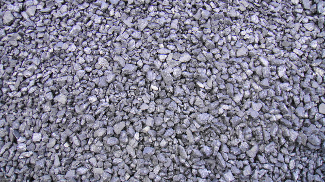 Góra drobnego, ciemnoszarego węgla kamiennego, z pojedynczym, jasnym kamykiem pośród nich.