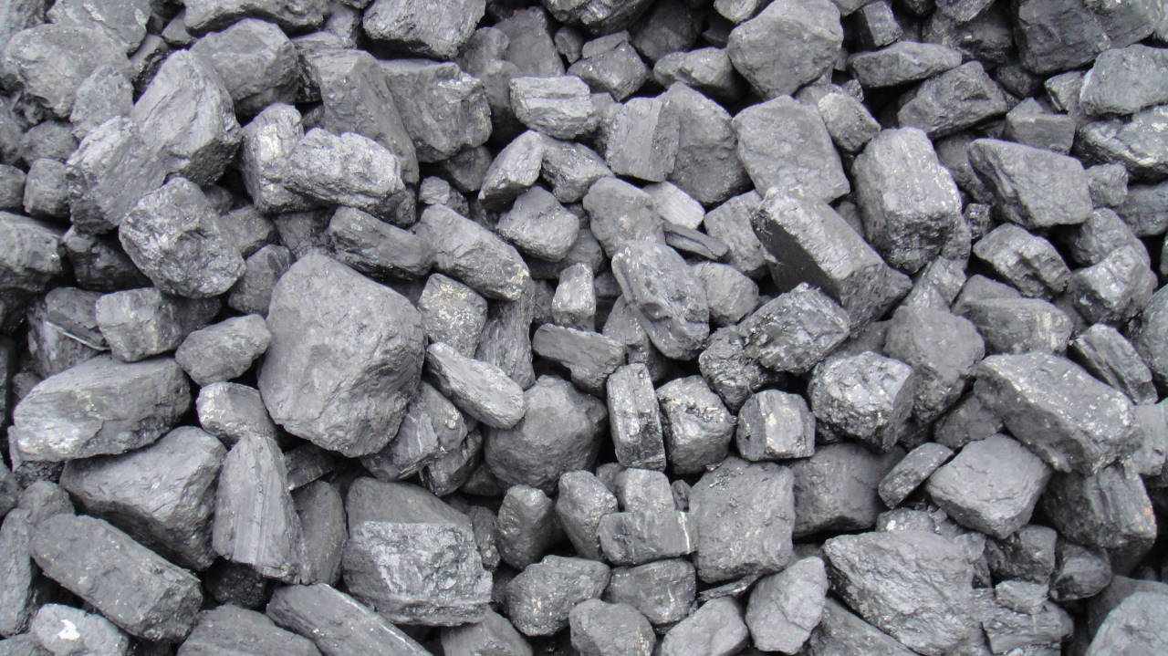 Kupa antracytu o nieregularnych kształtach, z widocznymi błyszczącymi powierzchniami i drobnymi pęknięciami, oświetlona naturalnym światłem.