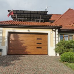 BRAM-BUD - Drewniana brama garażowa segmentowa z trzema poziomymi okienkami, zamontowana w Słupcu. Na dachu budynku powiewa flaga Polski.
