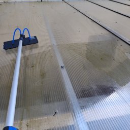 Das dekor - Czyszczenie zadaszenia z poliwęglanu w Dobrodzieniu za pomocą szczotki teleskopowej. Widoczne zabrudzenia i woda po myciu. Prace porządkowe na zewnątrz budynku.