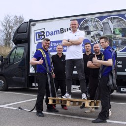 DB DamBus - Zespół firmy transportowej DamBus pozuje na tle busa z grafikami realizacji: wyburzenia, układanie kostki. Jeden z mężczyzn stoi na palecie, reszta daje kciuki w górę.
