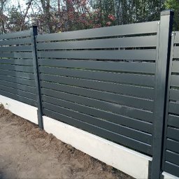 JDG OLEKSANDR VITVITSKYI - Nowoczesne, poziome ogrodzenie panelowe w kolorze grafitowym, osadzone na betonowej podmurówce. Widoczne słupki i poziome panele tworzące minimalistyczny design.