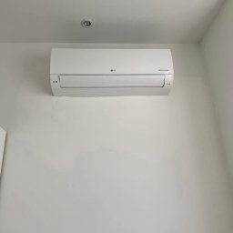 Vortex-montujemy komfort - Biały klimatyzator LG Dual Inverter zamontowany na jasnej ścianie, widoczny z dołu, z lampą sufitową w tle. Minimalistyczny design.