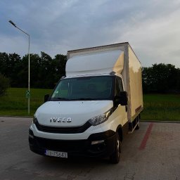 ProTrans - Biały samochód dostawczy Iveco z zabudową kontenerową, zaparkowany na kostce brukowej, na tle zieleni i pochmurnego nieba. Widoczny znak z zieloną strzałką.