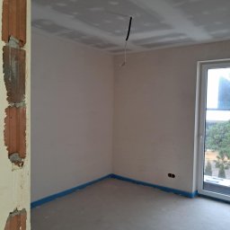 Dawid Panek - Surowe wnętrze w trakcie prac: ściany po szpachlowaniu, przygotowany sufit z płyt karton-gips, zabezpieczona podłoga folią. Widoczne niedokończone obramowanie drzwi.