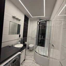 Wojciech Maćkowiak firma handlowo-usługowa - Nowoczesna łazienka z podświetlanym sufitem LED, kabiną prysznicową i marmurową podłogą. Minimalistyczny design z czarno-białymi akcentami i pralką w zabudowie.