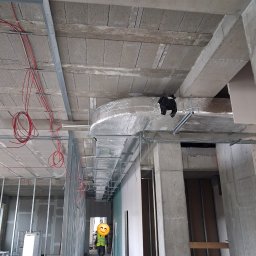 Thermiq - Montaż instalacji wentylacyjnej w surowym wnętrzu budynku. Widoczne przewody wentylacyjne, kable elektryczne i konstrukcja ścian działowych.