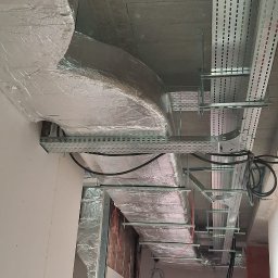 Thermiq - Sufit z widoczną instalacją wentylacyjną w srebrnej izolacji, koryta kablowe i przewody. Widok z dołu, surowy stan wykończenia wnętrza.