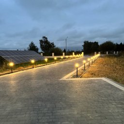 Usługi Elektryczne Maciej Krasnodębski - Oświetlona ścieżka z kostki brukowej prowadząca do domu z panelami słonecznymi w pochmurny dzień. Lampy ogrodowe wzdłuż ścieżki.