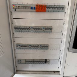 Usługi Elektryczne Maciej Krasnodębski - Rozdzielnica elektryczna z widocznymi bezpiecznikami i wyłącznikami, zamontowana w białej obudowie. Widoczne oznaczenia producentów Hager i KVR.