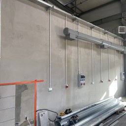 PRIME SERVICE - Szara ściana z poprowadzonymi białymi rurami instalacji elektrycznej i wentylacyjnej. Widoczne gniazdka, puszki i przewody. Na podłodze leżą rury wentylacyjne.