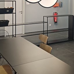 GLE Grzegorz Łachański uslugi elektryczne - Trzy okrągłe lampy LED z czarnymi ramami, zawieszone na różnych wysokościach nad długim, ciemnym stołem w minimalistycznym wnętrzu biurowym z regałami.