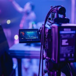 Blue tn sp. j - Profesjonalna kamera filmowa Blackmagic z podglądem nagrywanego koncertu w fioletowo-niebieskim oświetleniu scenicznym, ustawiona na statywie.