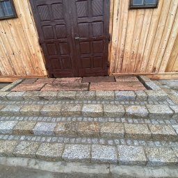 V-I BrukGarden - Granitowe schody wejściowe do drewnianego budynku z brązowymi drzwiami, świeżo po ułożeniu, z widocznymi narzędziami i elementami rusztowania w tle.