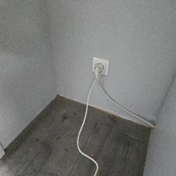 Nova Clean - Szary kąt pokoju z gniazdkiem elektrycznym i wpiętym kablem. Widoczne ślady kurzu na podłodze. Minimalistyczne wnętrze w odcieniach szarości.