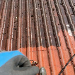 Panel Cleaner - Częściowo umyty dach z czerwonej dachówki, widoczne zabrudzenia i mech. Różnica między czystą a brudną powierzchnią. Ujęcie z perspektywy osoby wykonującej czyszczenie.