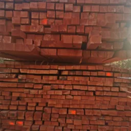 Ułożone warstwami, suche, czerwono-brązowe kantówki z drewna z widocznymi pomarańczowymi oznaczeniami na niektórych elementach.