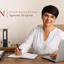 Biuro Rachunkowe AN Agnieszka Niczyporuk - Uśmiechnięta kobieta w białej koszuli, siedząca przy biurku z laptopem i notatnikiem, pisząca długopisem. W tle logo 'AN Biuro Rachunkowe Agnieszka Niczyporuk'.